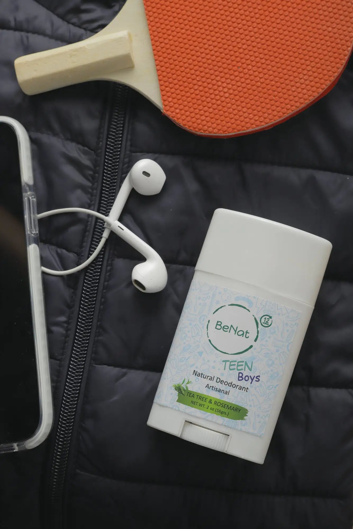 All-natural deodorant for kids placed next to a phone and earphones on a quilted jacket.